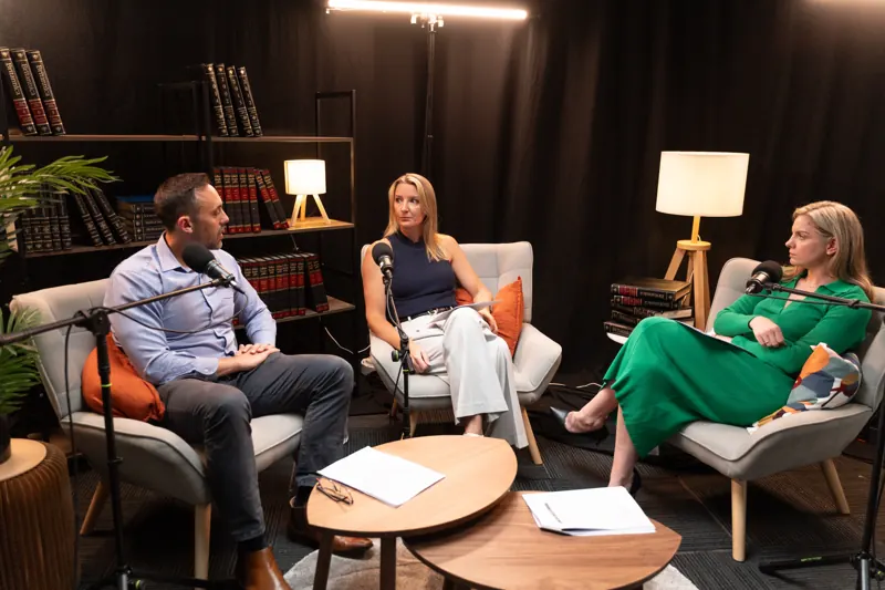 Three people talking in armchairs on the lounge set, lamps and a bookshelf behind them