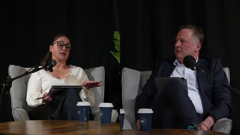 Two Ryker Capital panellists mid-conversation in armchairs, takeaway coffees on the table in front of them