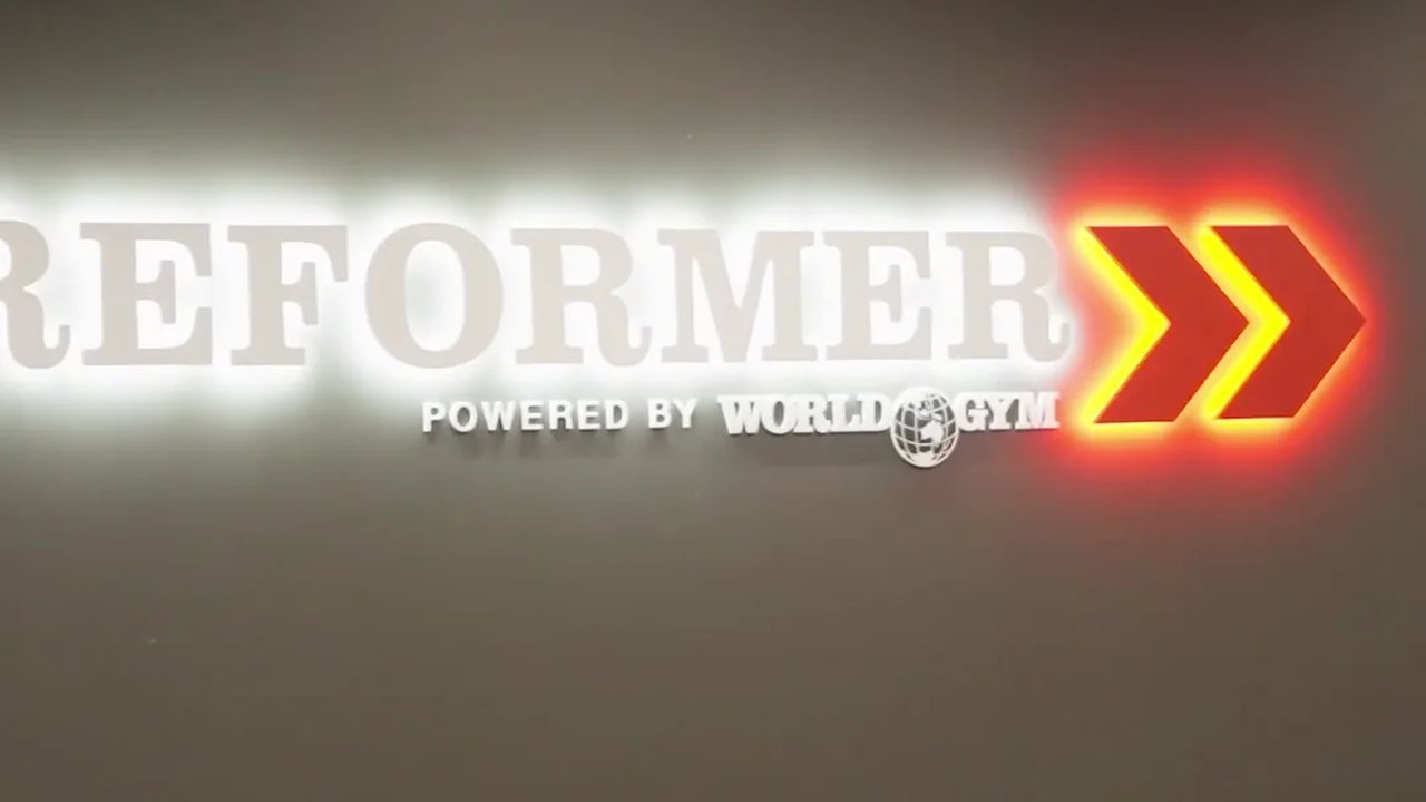 The Reformer studio sign, powered by World Gym, lit above the machines.