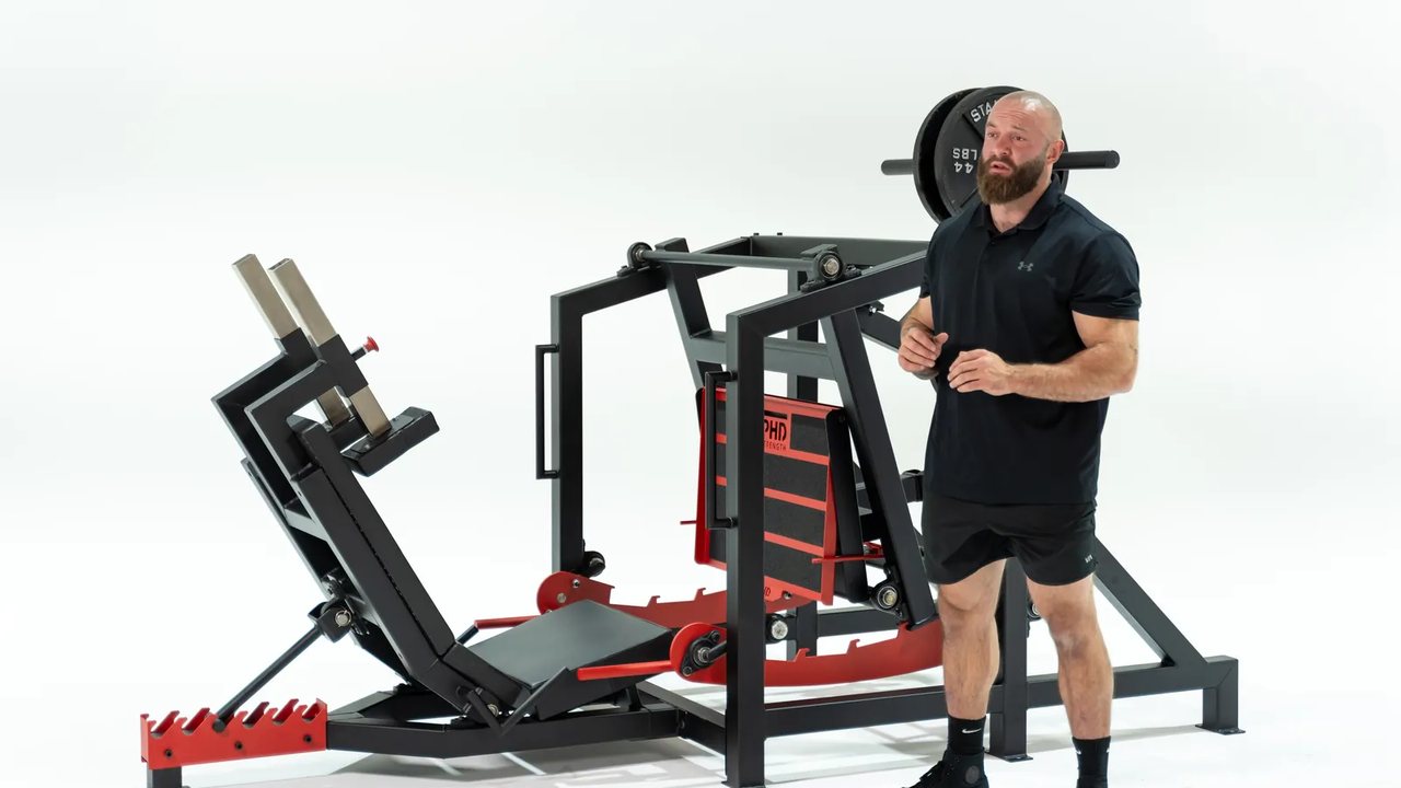 A PHD Strength machine photographed on a white backdrop, with a trainer standing beside it.