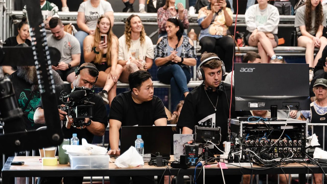 A live production desk at a One Strength event: camera operator, director and vision mixer, with the crowd behind.