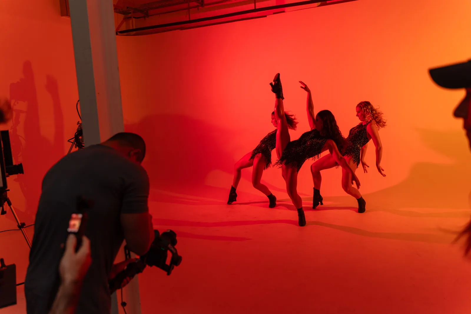 Camera operator filming dancers against a red backdrop in the studio