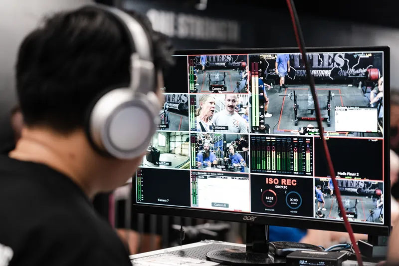An operator at the stream desk during a One Strength powerlifting meet, every camera on the multiview monitor